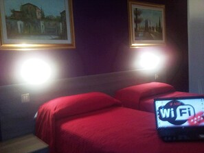 A hotel room with two beds, a laptop displaying a WiFi symbol, and two framed pictures on the wall. - Hotel Bristol (Sesto San Giovanni)