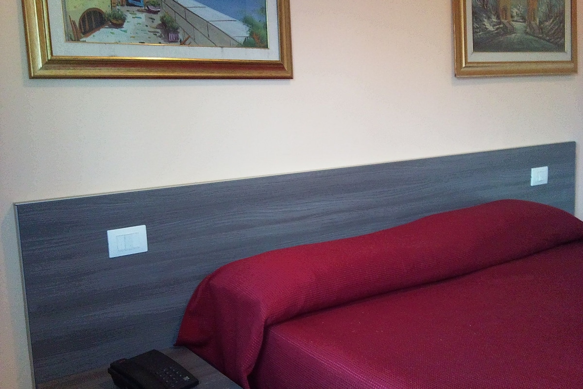 A hotel room with a bed, a nightstand, and two framed pictures on the wall.