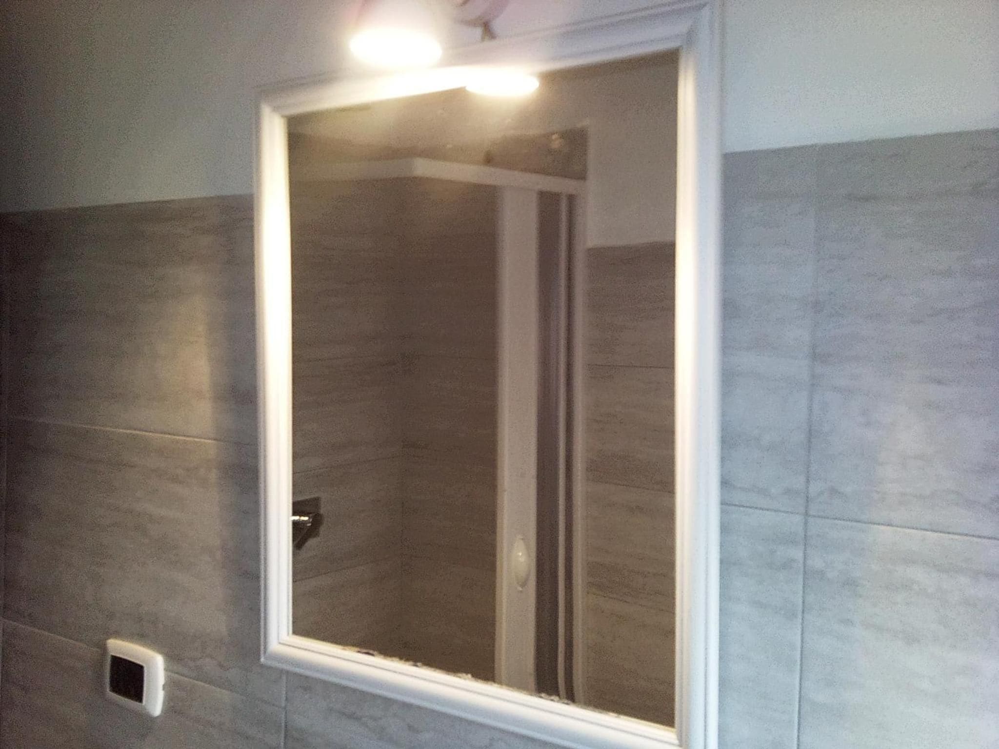A bathroom with a glass shower enclosure, a white door, and a light fixture above the mirror.