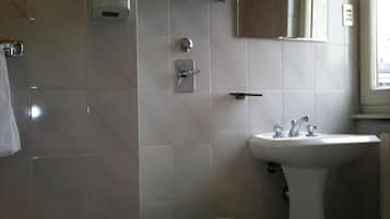 Un baño con inodoro, lavamanos y un estante de vidrio sobre el espejo.