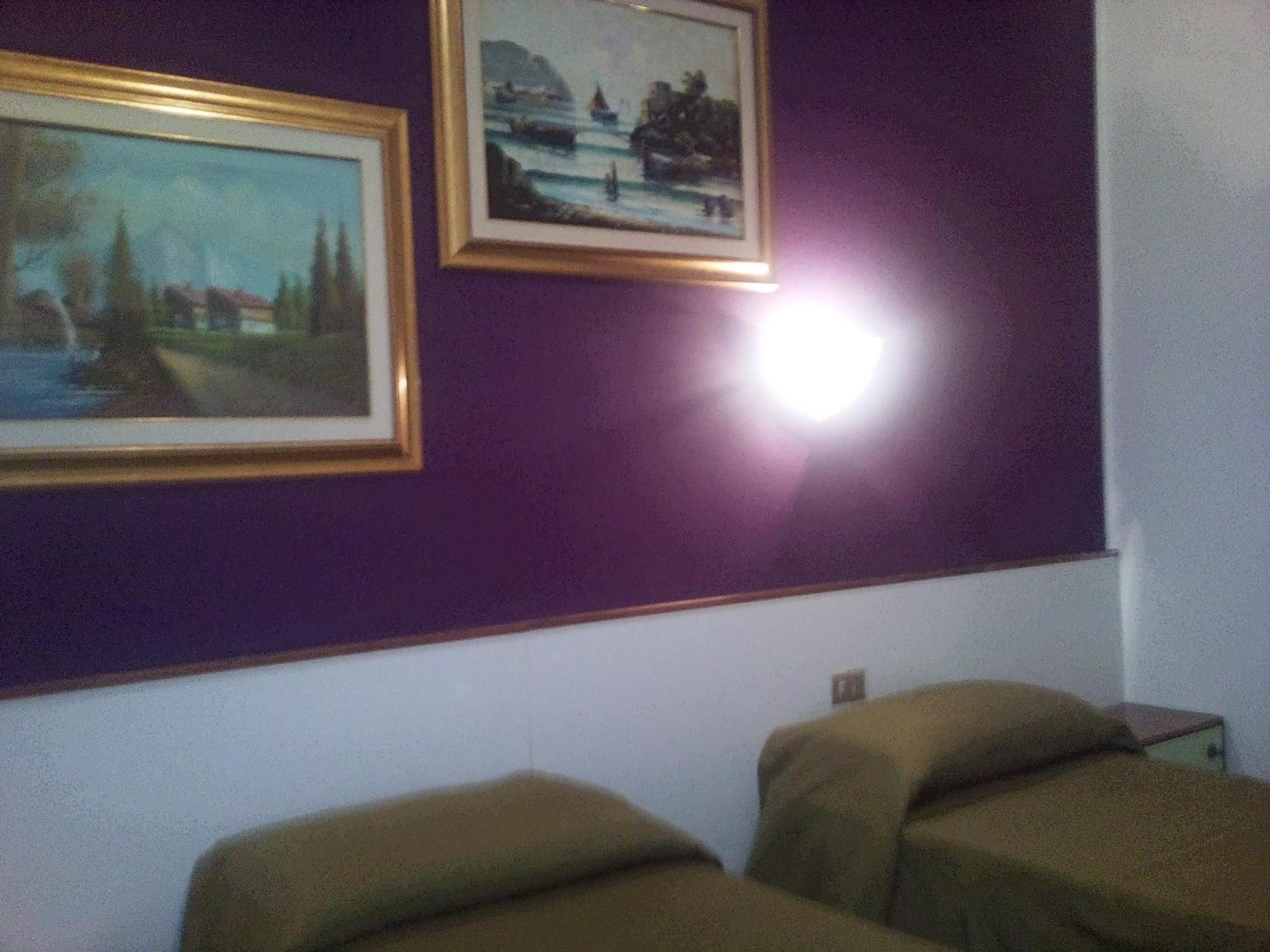 Ein Zimmer mit zwei Betten, einer violetten Wand und zwei gerahmten Bildern.