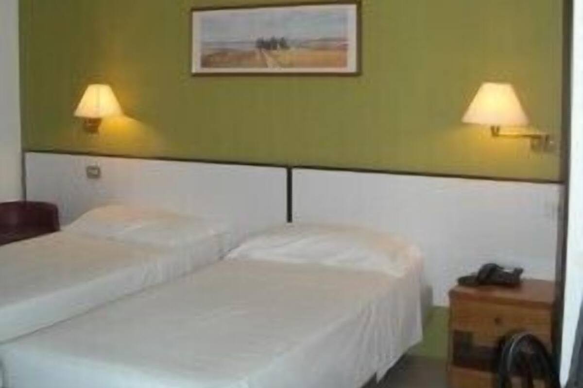 A hotel room with two single beds, a nightstand with a lamp, and a framed picture on the wall.