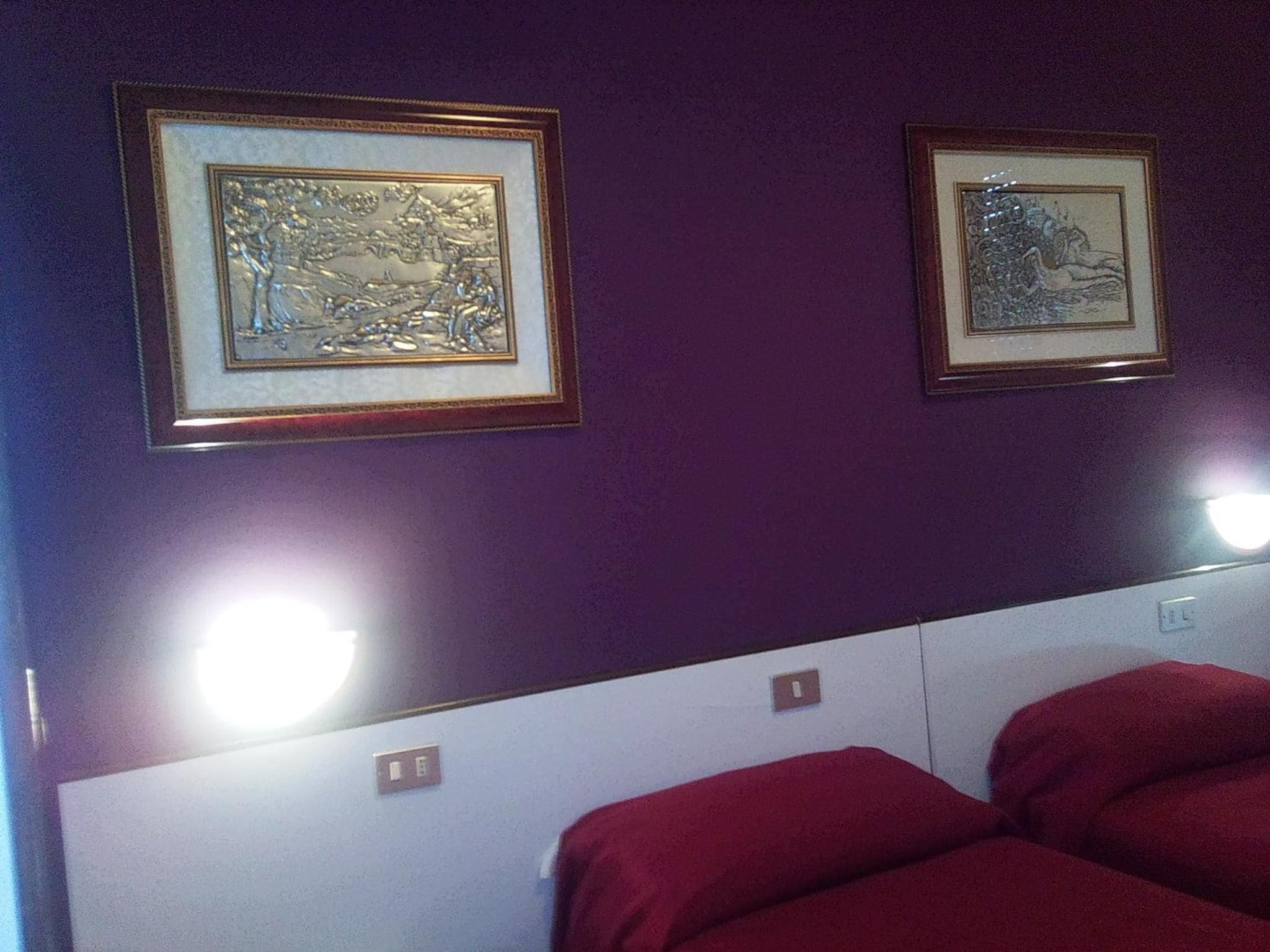 A room with two framed artworks on the wall and a bed with red bedding.
