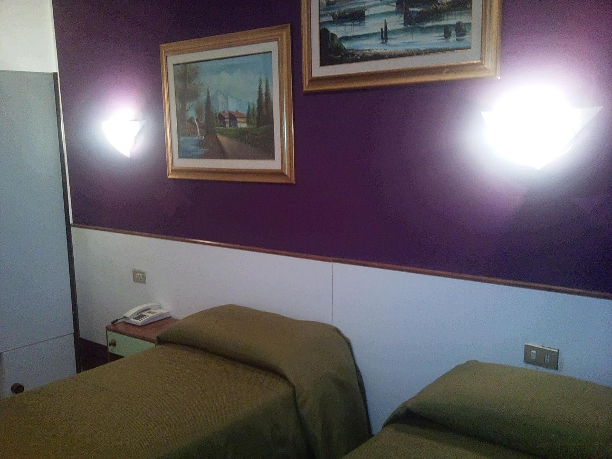 Ein Hotelzimmer mit zwei Betten, einem Nachttisch mit Telefon und zwei gerahmten Bildern an der Wand.