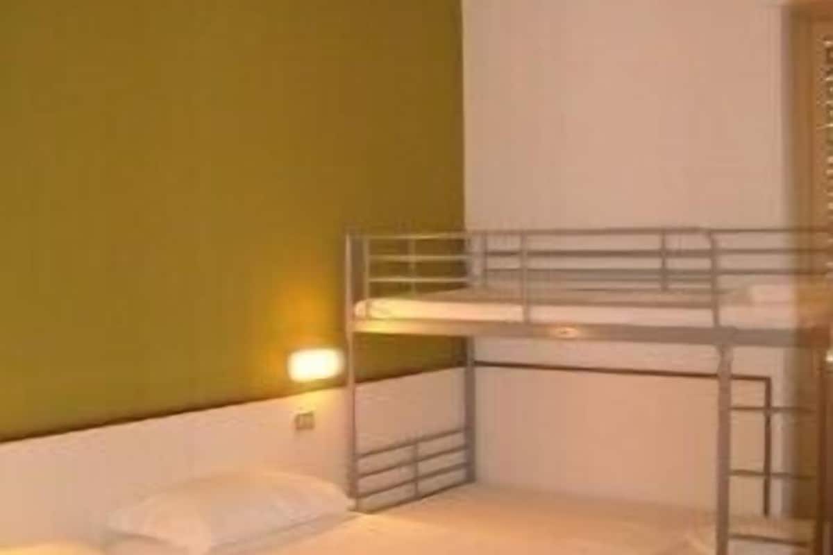 A hotel room with two beds, a bunk bed, and a single light fixture.