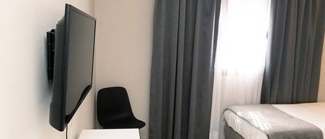 A hotel room with a bed, a desk, a chair, a TV, and curtains.