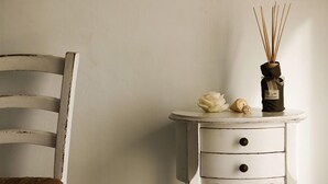 A white, distressed wooden chair with a woven seat next to a white, distressed side table with two drawers. - Hotel Albatros Varigotti (Finale Ligure)