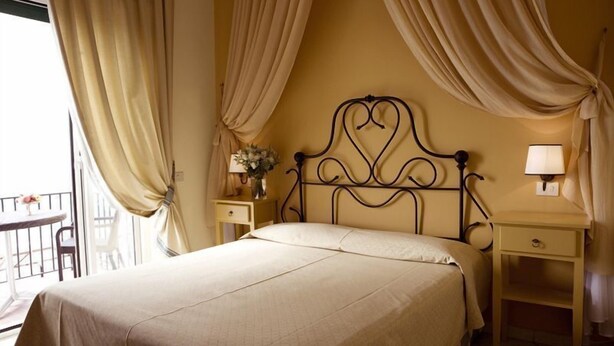 A hotel room with a bed, a nightstand, a lamp, and a view of the outside balcony. - Hotel Albatros Varigotti (Finale Ligure)