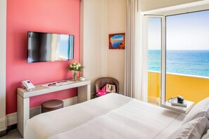 Ein Hotelzimmer mit Bett, Schreibtisch mit Telefon, Stuhl, Wandfernseher und einem Fenster mit Meerblick.