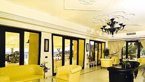 A spacious lobby with yellow sofas, a black armchair, and a glass coffee table. - Hotel Albatros Varigotti (Finale Ligure)