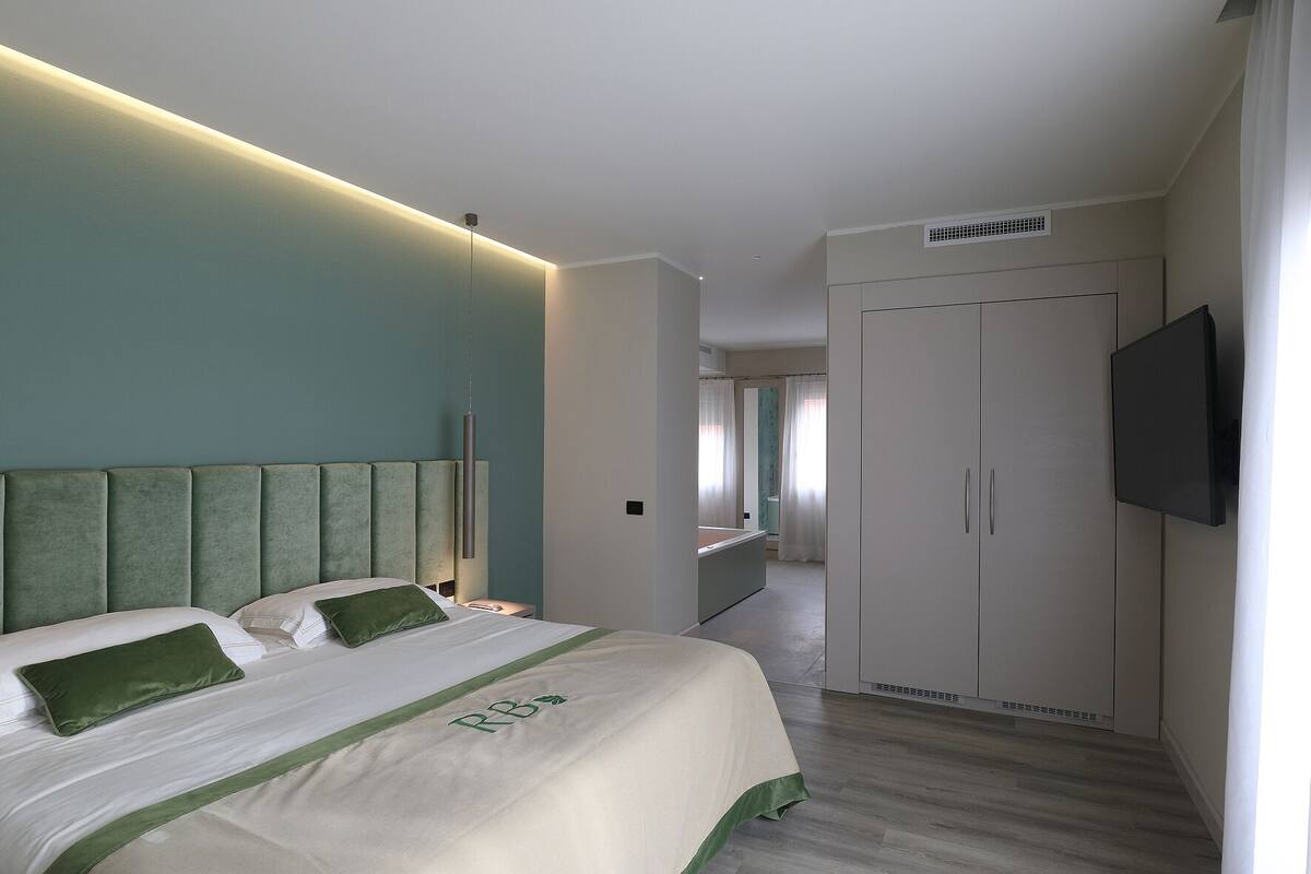A modern hotel room with a large bed, a flat-screen TV, and a walk-in closet.