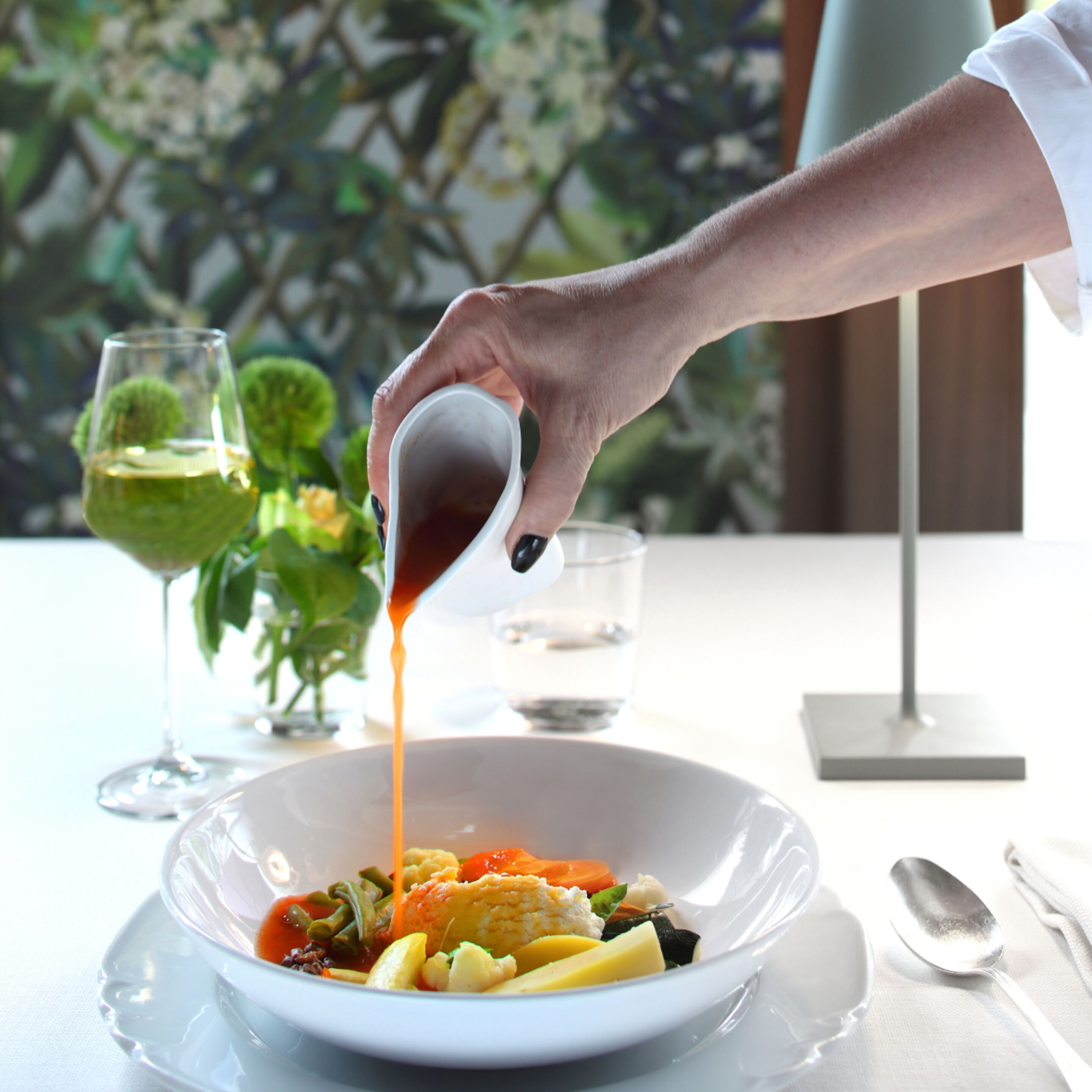 Una persona sirviendo salsa sobre un plato de verduras y pasta.