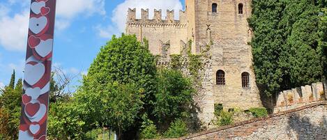 Una torre histórica con fachada de piedra y ventanas de arco, rodeada de exuberante vegetación.