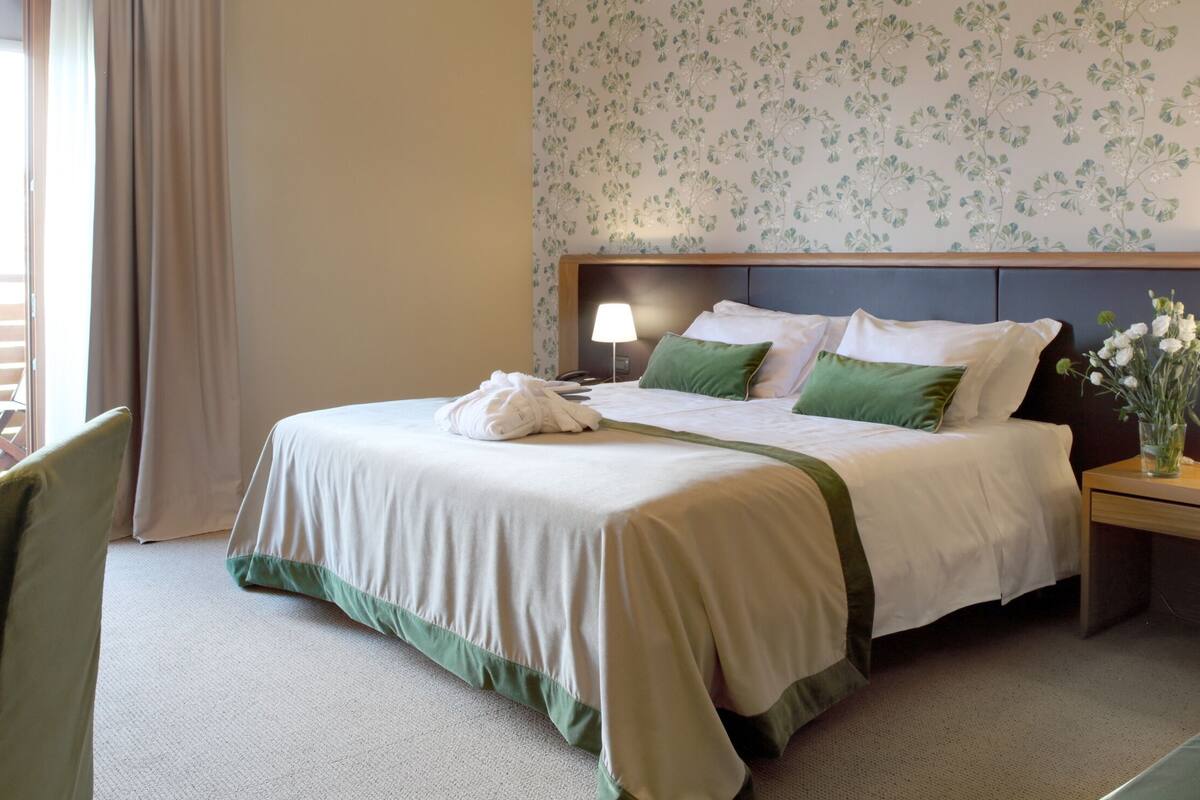A neatly made bed with a green and white bedspread, two bedside lamps, and a nightstand with a vase of flowers.