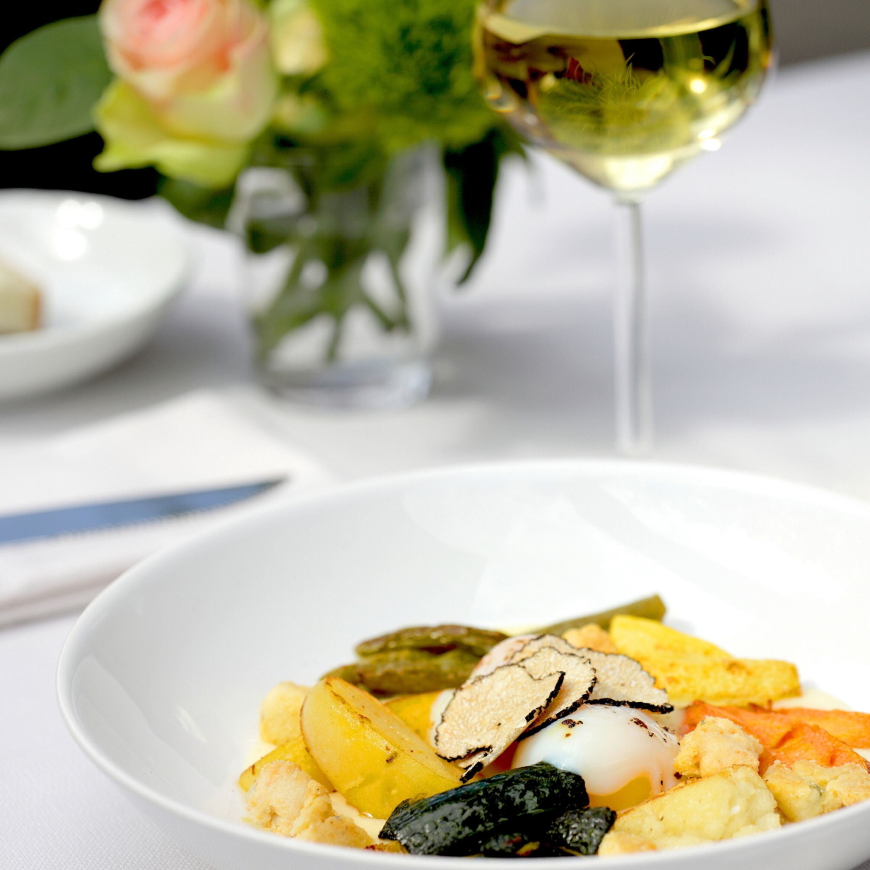 Un tazón blanco con diversos alimentos, incluyendo papas, un huevo pochado y algunas verduras.