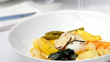 Un tazón blanco con diversos alimentos, incluyendo papas, un huevo pochado y algunas verduras.