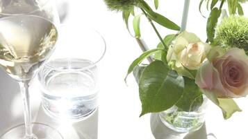 Una copa transparente de vino blanco, un vaso de agua y un florero con rosas y follaje verde.