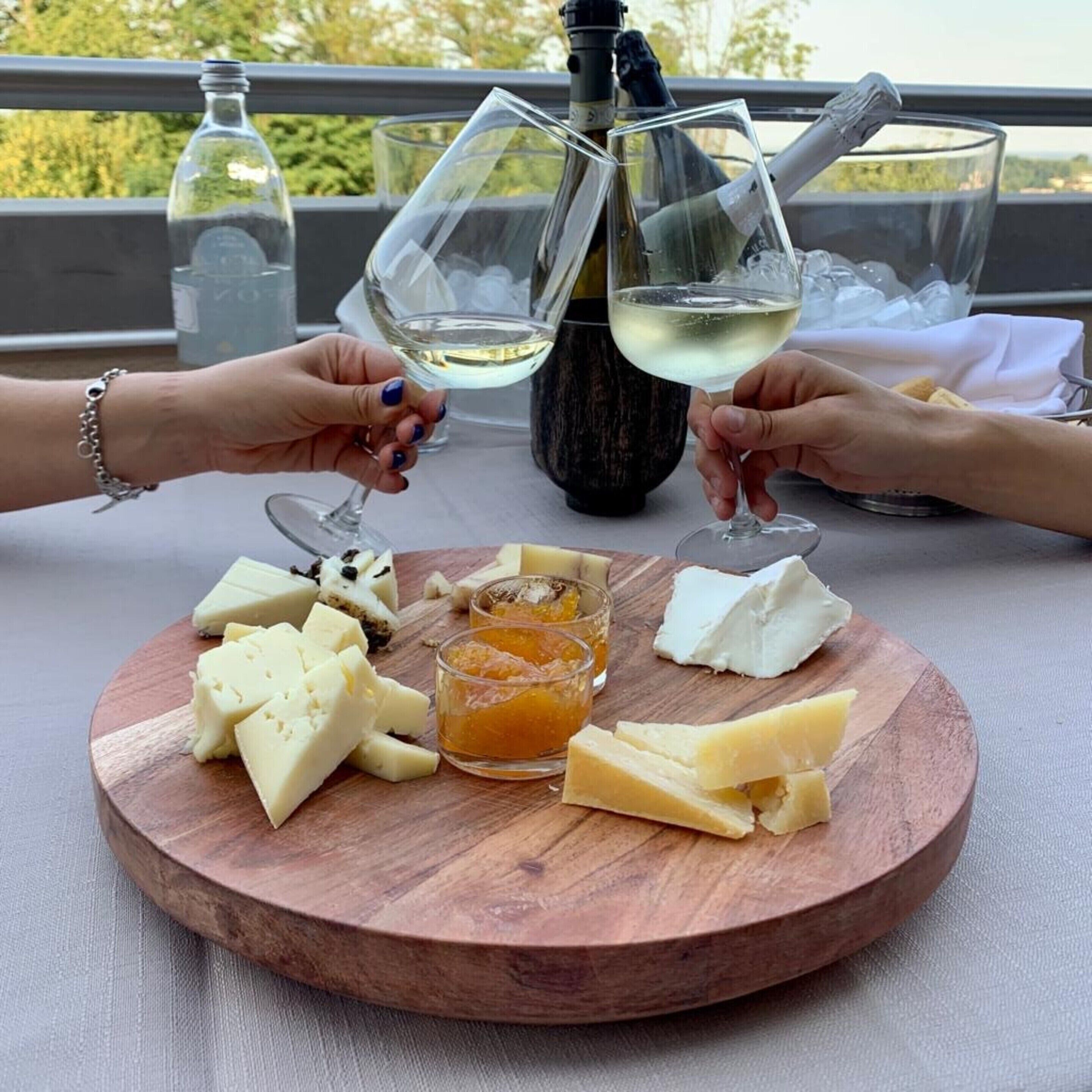 Una tabla de madera con queso, una botella y copas en un balcón.