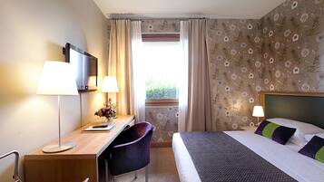 A hotel room with a bed, desk, chair, TV, and window with curtains.