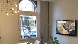 A modern dining area with a table and chairs, a decorative light fixture, a potted plant, and a television mounted on the wall. - Hotel d'Amsterdam (Amsterdam)