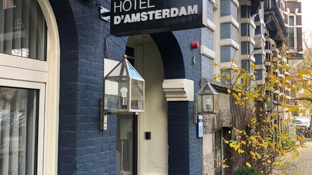A hotel entrance with a black sign reading "HOTEL D'AMSTERDAM," a glass door, and a small potted plant. - Hotel d'Amsterdam (Amsterdam)