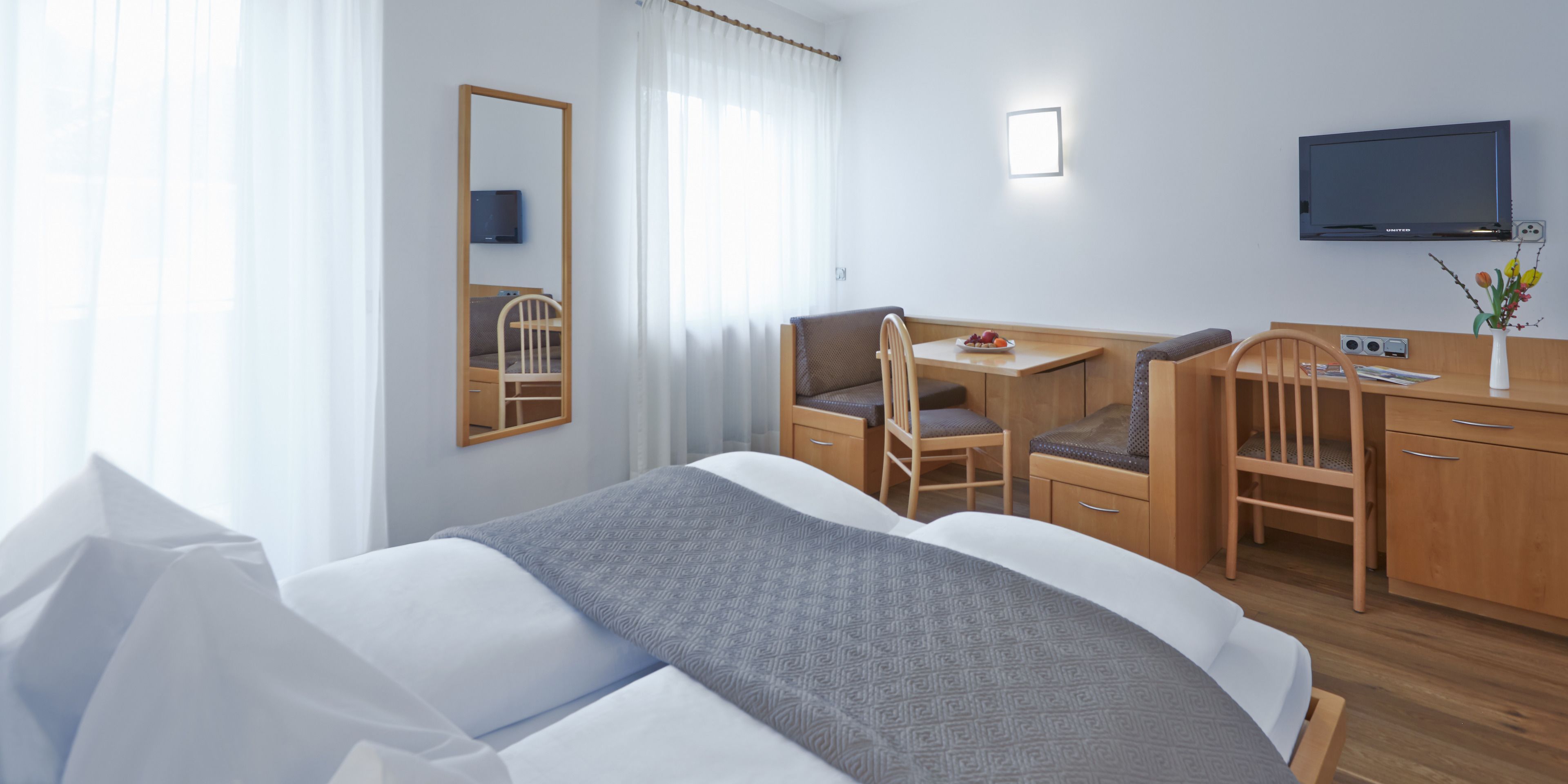 A hotel room with a bed, a desk with a chair, a television, and a mirror.