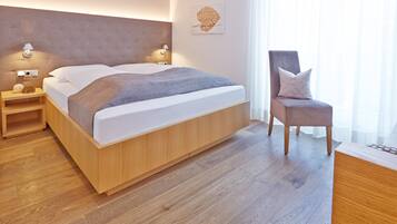 Un dormitorio moderno con una cama grande, lámparas de noche, una mesita de noche de madera, una silla y un ventanal con cortinas traslúcidas.