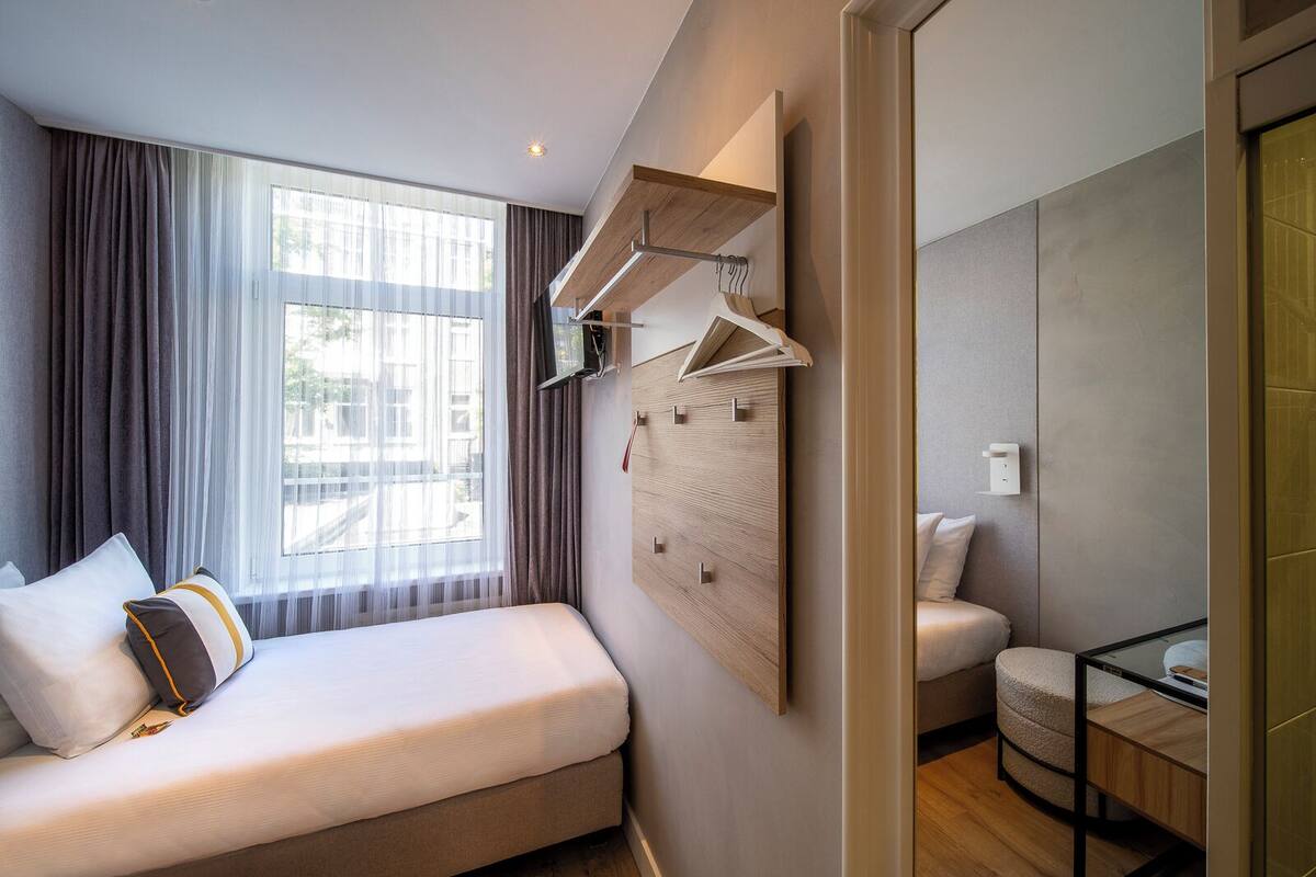 A modern hotel room with a large bed, a seating area, and a wardrobe with a mirror.