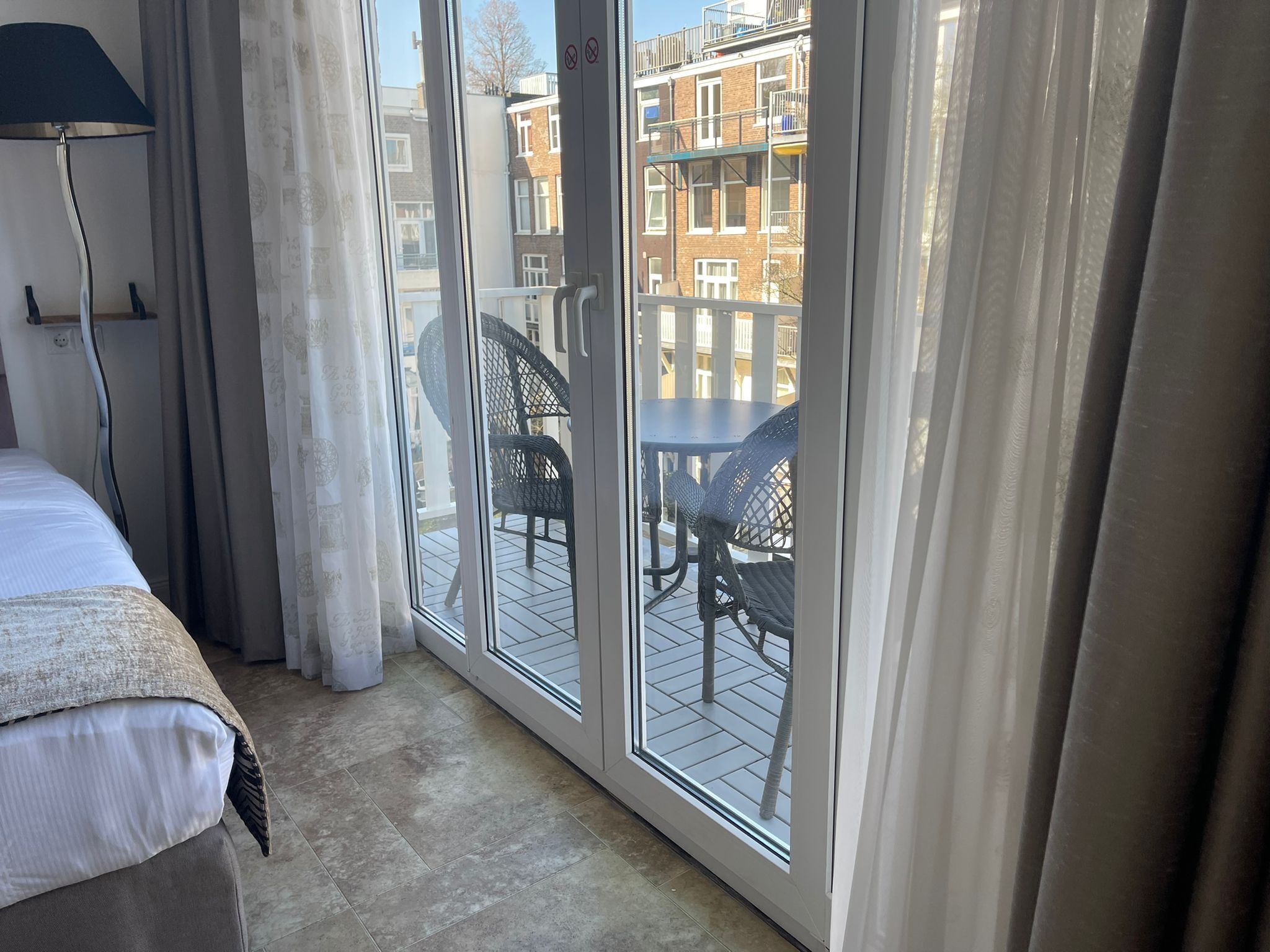 A hotel room with a bed, a desk, a chair, and a balcony with a table and chairs.