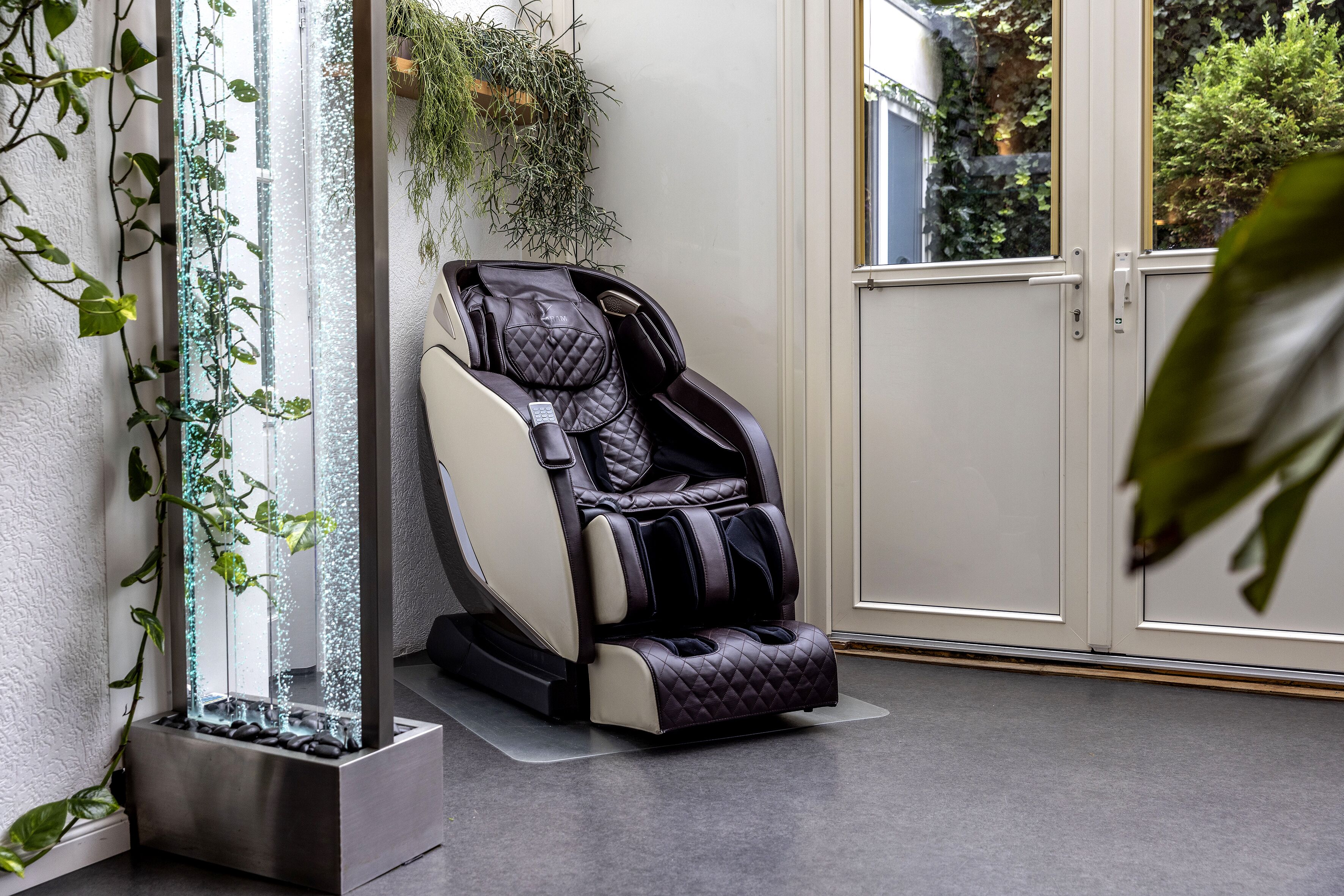 A massage chair in a room with a glass water feature and a view of greenery outside.