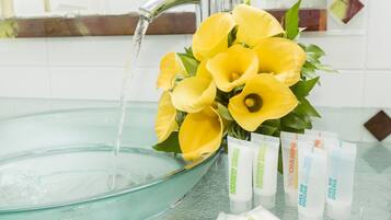 A bathroom sink with running water, a bouquet of yellow flowers, and several tubes of lotion.