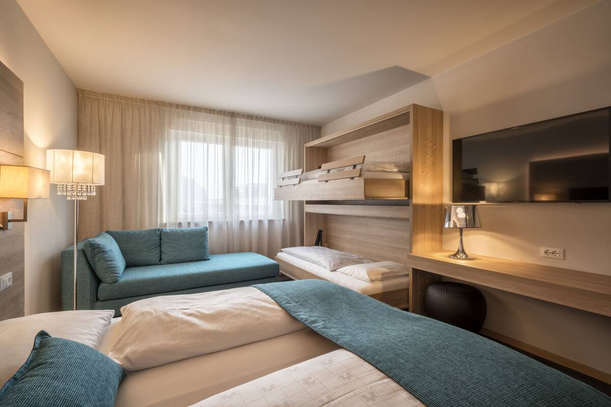 Habitación de hotel con sofá, dos camas, televisión, escritorio y ventana con cortinas.