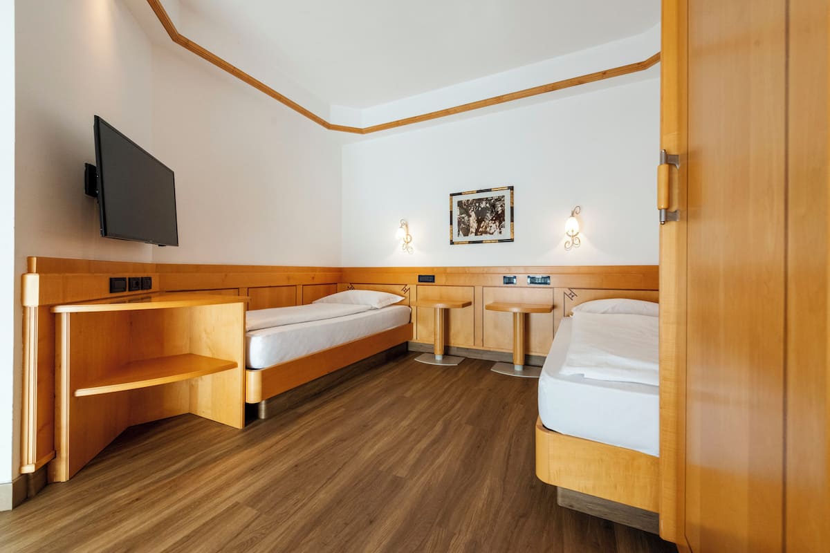Una habitación de hotel compacta con dos camas individuales, un escritorio, una mesita pequeña, un televisor y un cuadro en la pared.