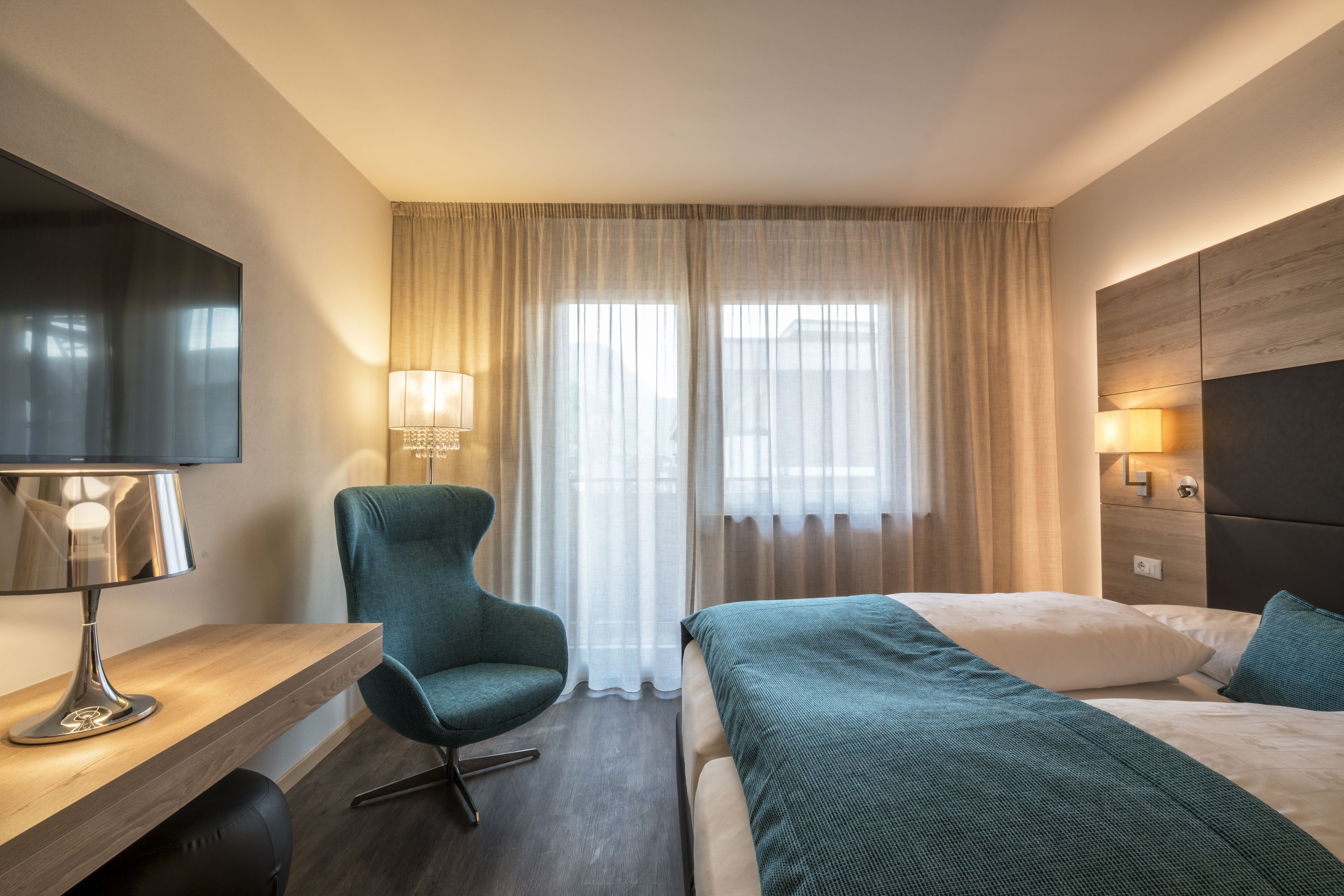Ein Hotelzimmer mit Bett, Schreibtisch mit Lampe, Stuhl und Fernseher.