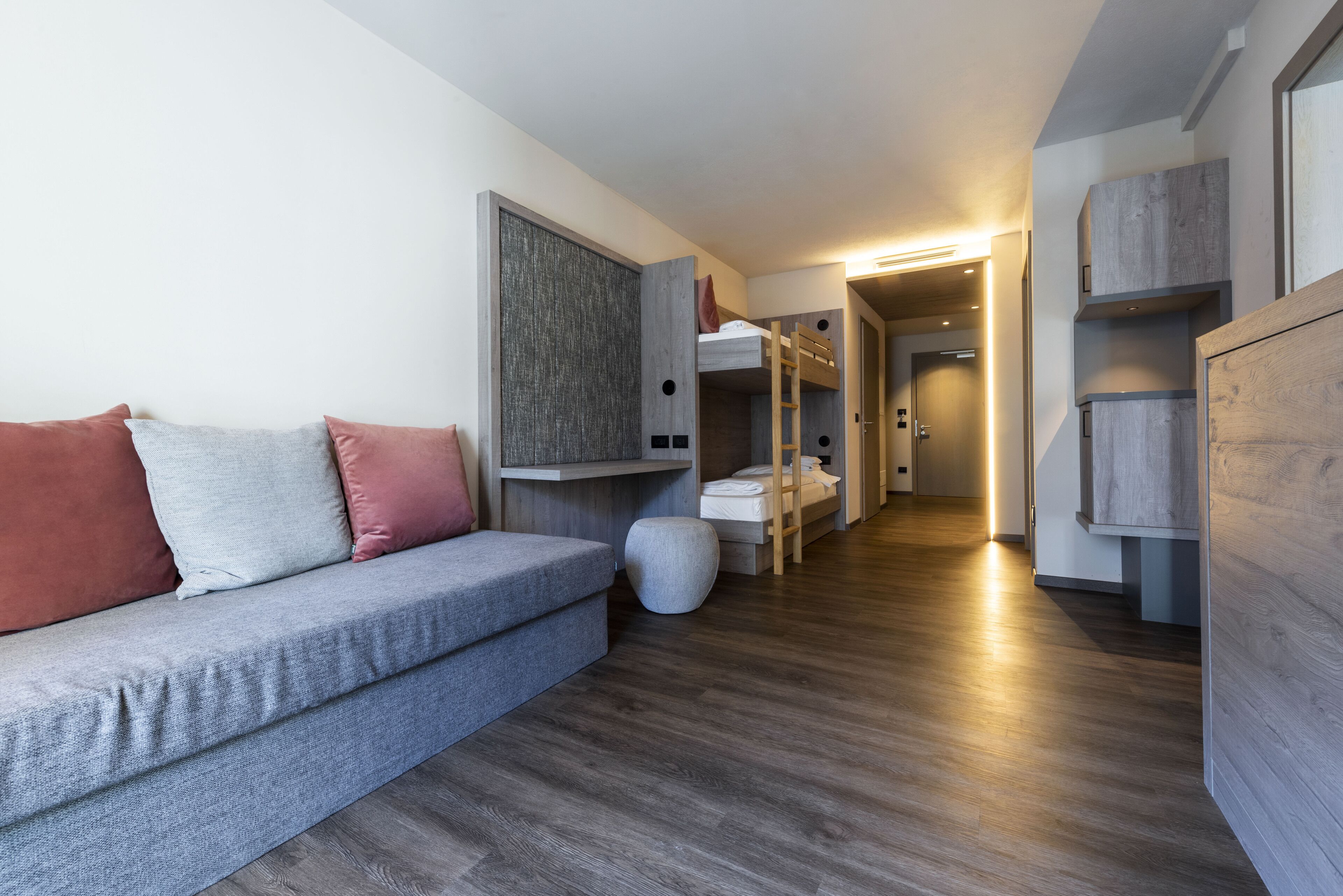 A modern, compact room with a grey sofa, a bunk bed, and a wooden wardrobe.