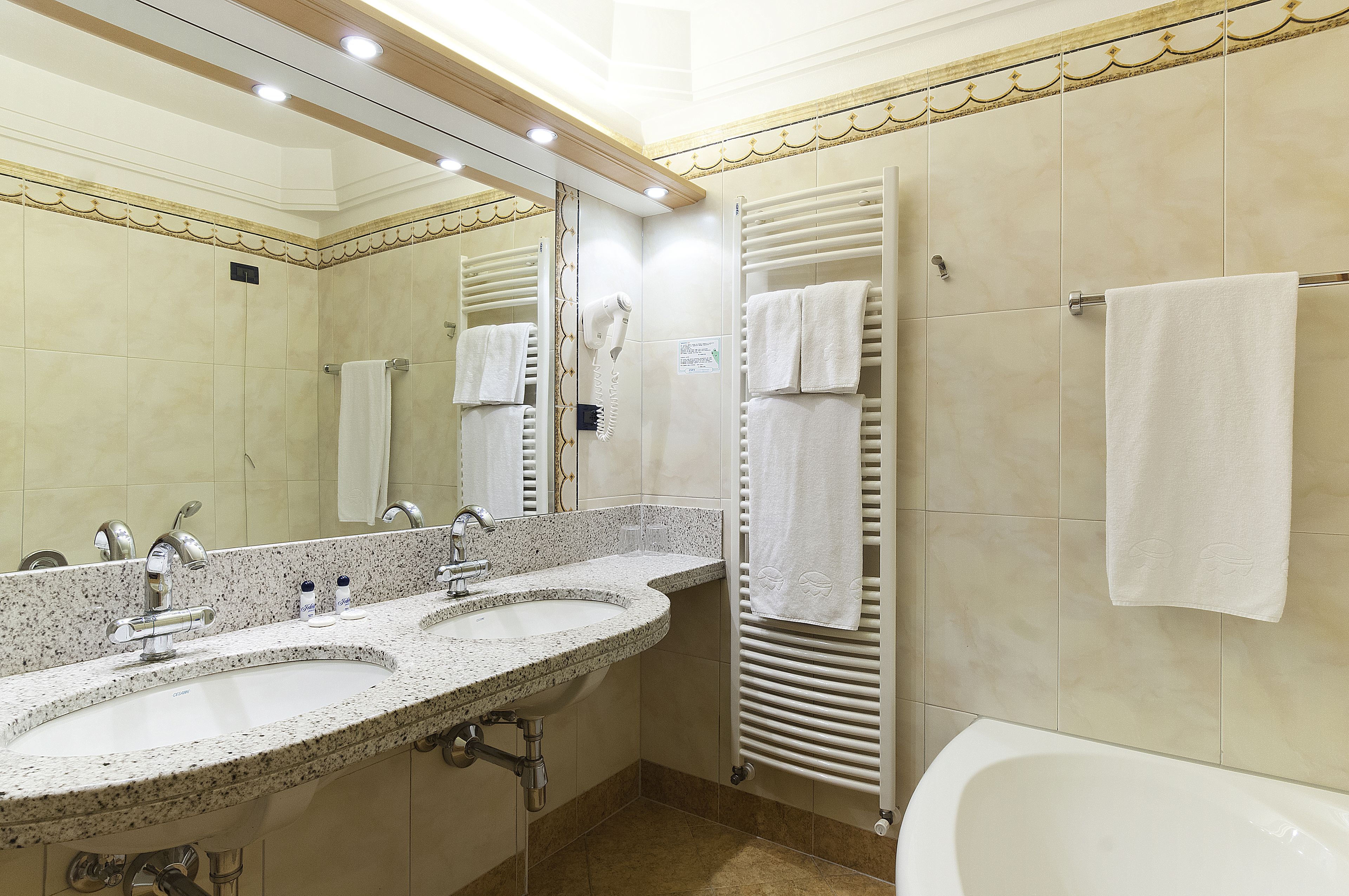 A hotel bathroom with two sinks, a large mirror, a hairdryer, and a bathtub.