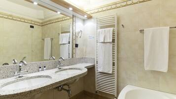 A hotel bathroom with two sinks, a large mirror, a hairdryer, and a bathtub.