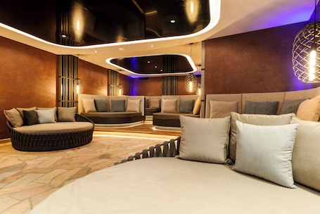 A modern lounge area with a stone floor, multiple seating options including sofas and a circular bench, and ambient lighting.. Ideal Park