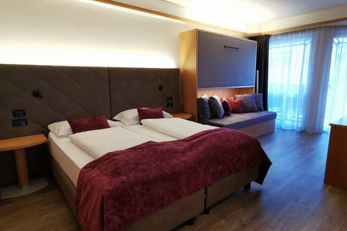 Habitación de hotel con una cama grande, un sofá, un televisor y un ventanal con cortinas.