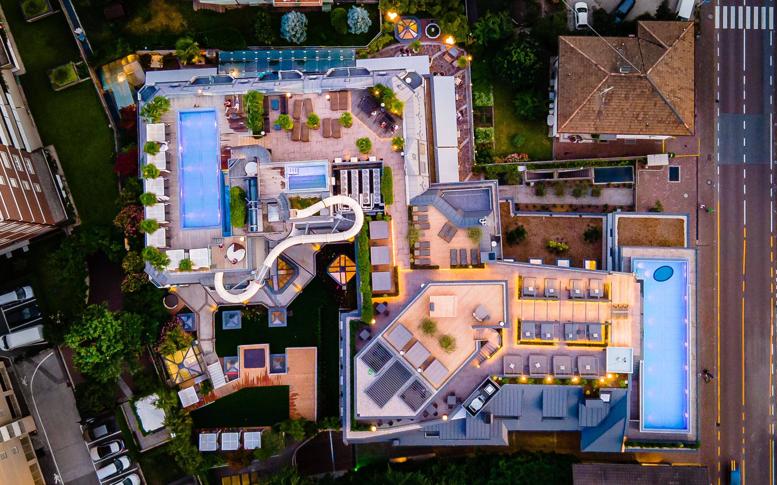 An aerial view of a hotel with multiple swimming pools, outdoor seating areas, and a rooftop terrace.