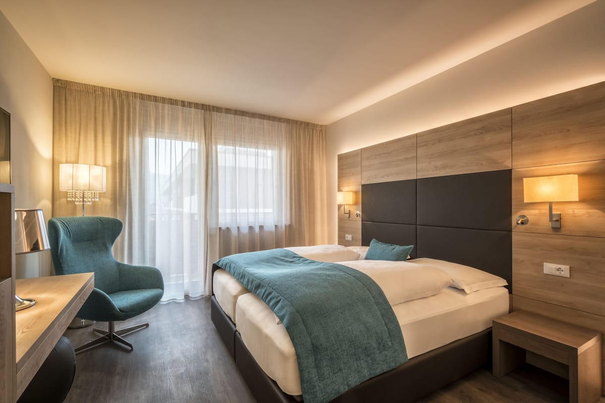 Una habitación de hotel moderna con una cama grande, un escritorio con silla y una mesita de noche.