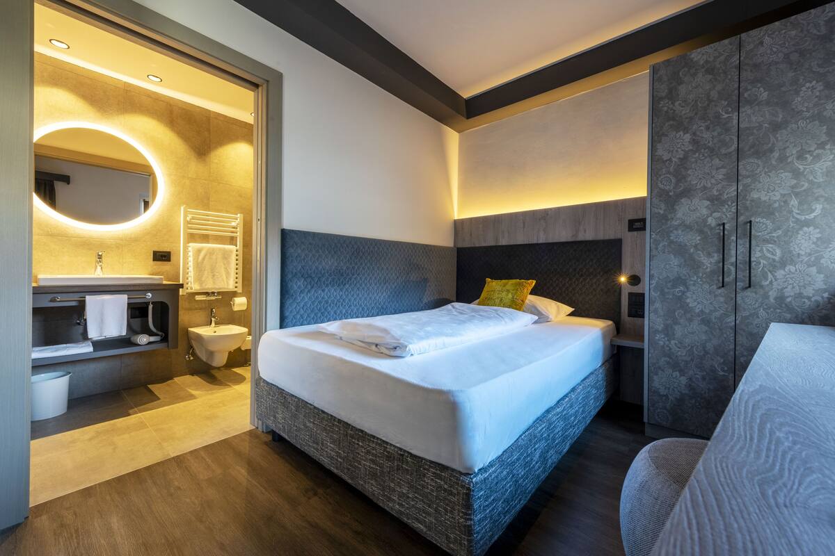 Una habitación de hotel moderna con una cama grande, tocador empotrado, espejo redondo y una zona de estar separada.