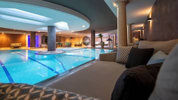 Een binnenzwembad met loungegedeeltes, een plafond met dakramen en een modern interieur.
