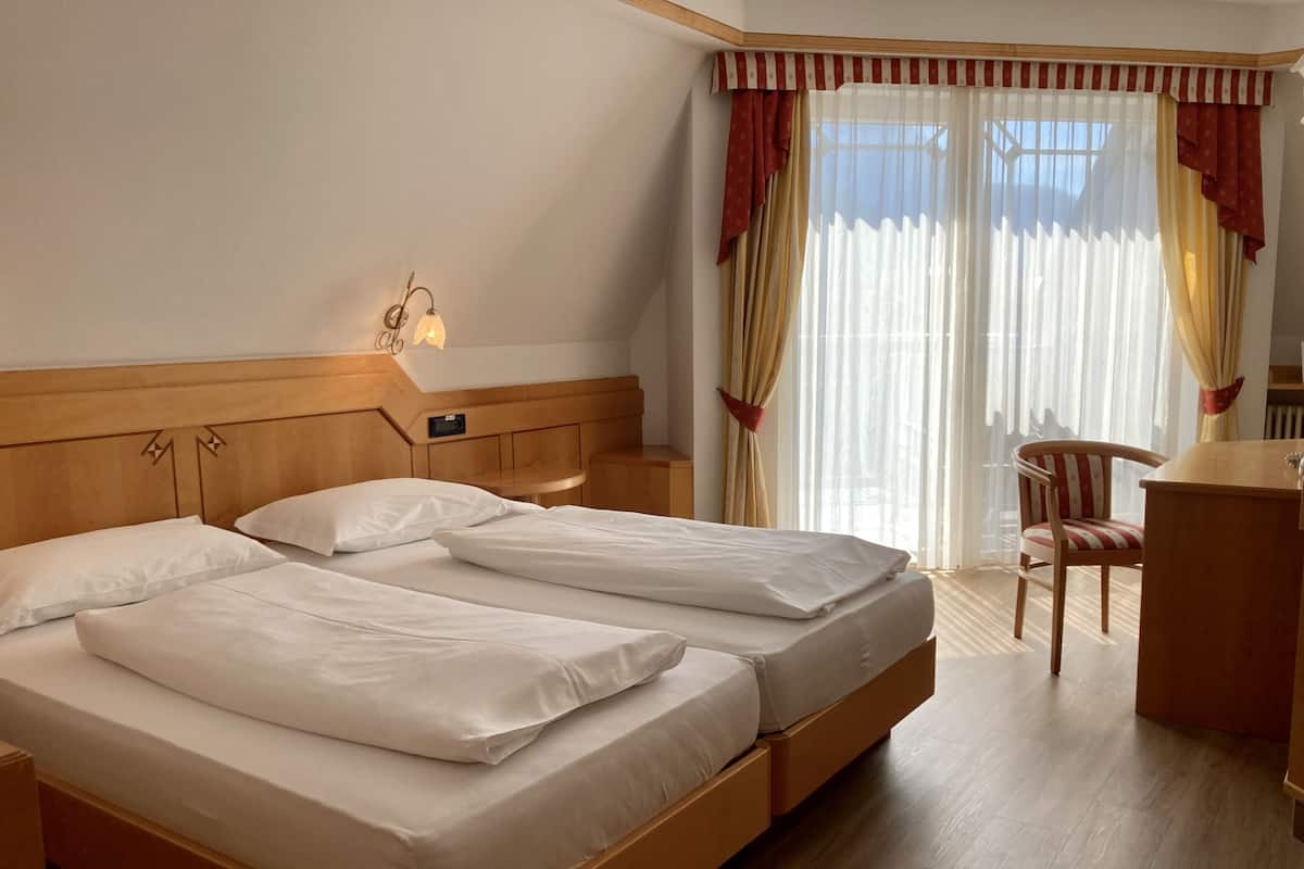 Una habitación de hotel con dos camas, un escritorio, una silla y un ventanal con cortinas.