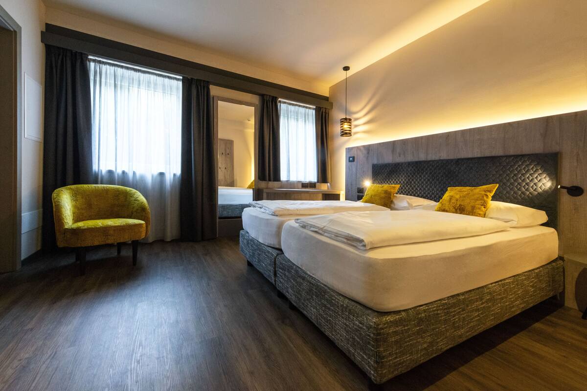 Una habitación de hotel con una cama grande, una silla y un ventanal con cortinas.