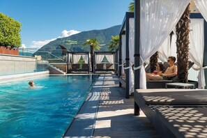 A pool area with a view of mountains, wooden deck, and lounge chairs.