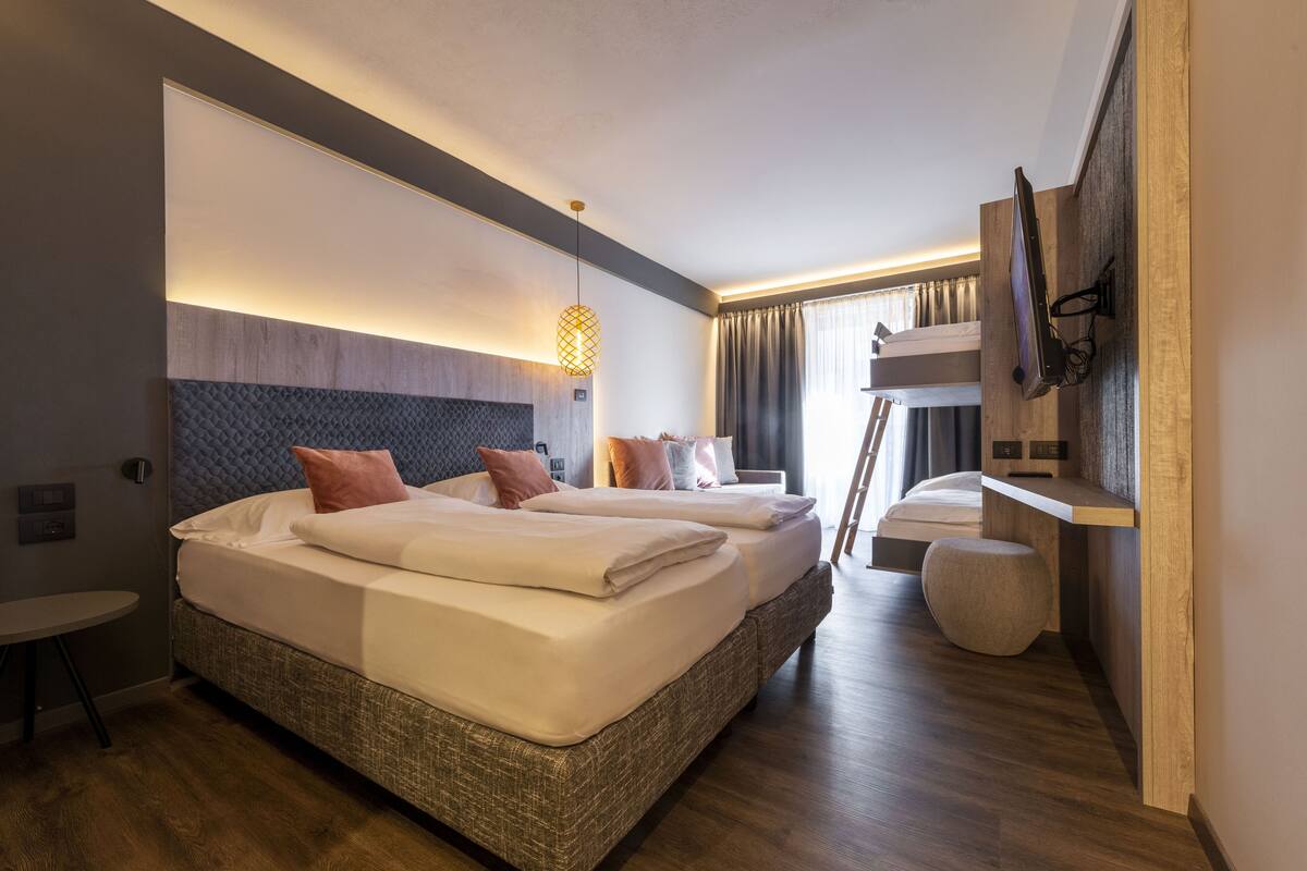 Una habitación de hotel moderna con dos camas, un escritorio pequeño, un televisor en la pared y un balcón con cortinas.