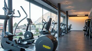 A gym with cardio machines and a view of mountains through large windows.