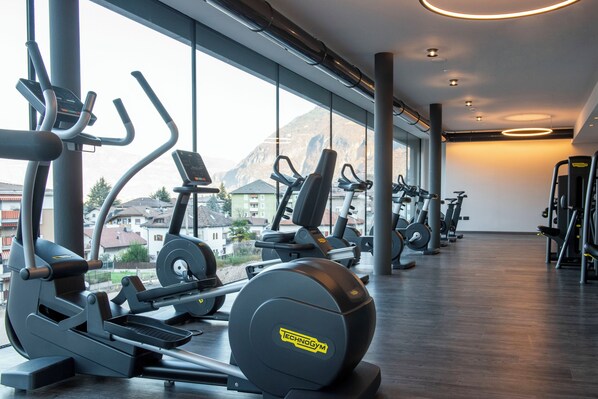 A gym with cardio machines and a view of mountains through large windows.