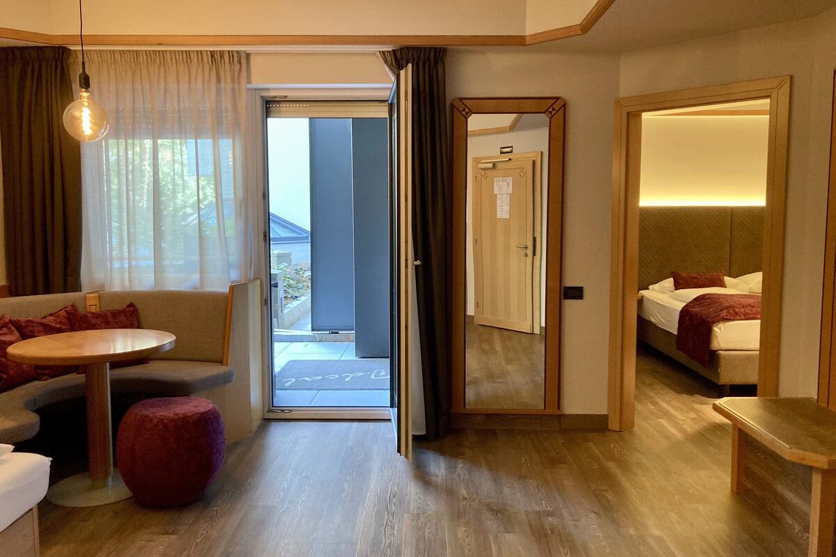 Habitación de hotel con sofá, una mesita, un reposapiés rojo, cama con cabecero y un espejo.